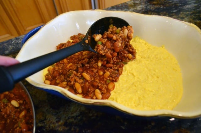 The chili is spooned over the top of the cornbread mixture in the baking dish.