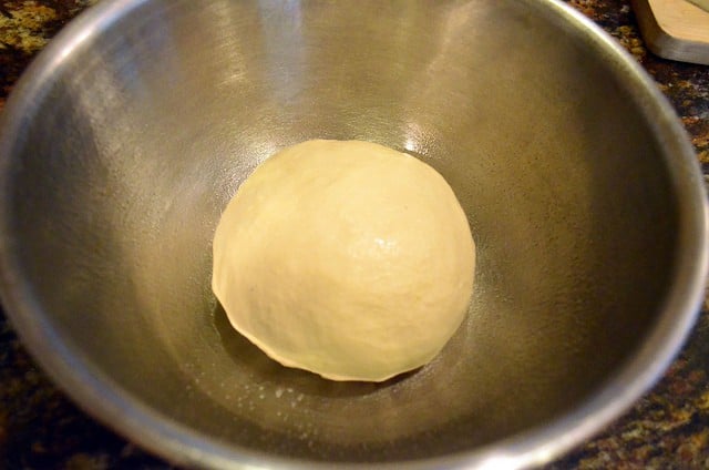 Bread dough shaped into a ball inside of a large bowl.