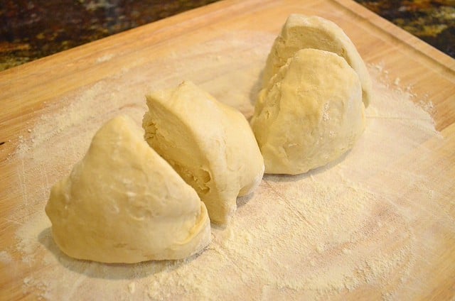 The bread dough, cut into 4 pieces, sitting on a cutting board covered with flour.