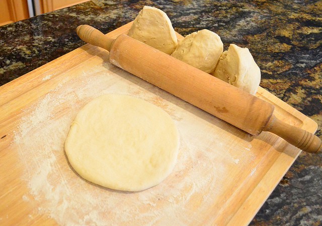 One of the pieces of bread dough rolled into a flat circle with a rolling pin.