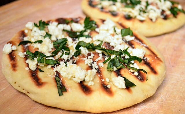 A close up of flatbread with feta and basil on top.