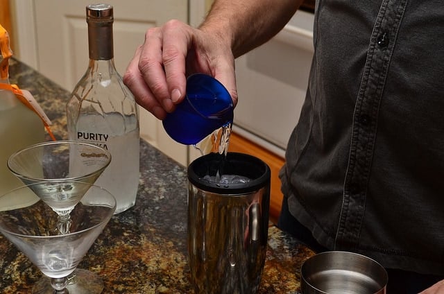 Vodka is poured into a shaker filled with ice.
