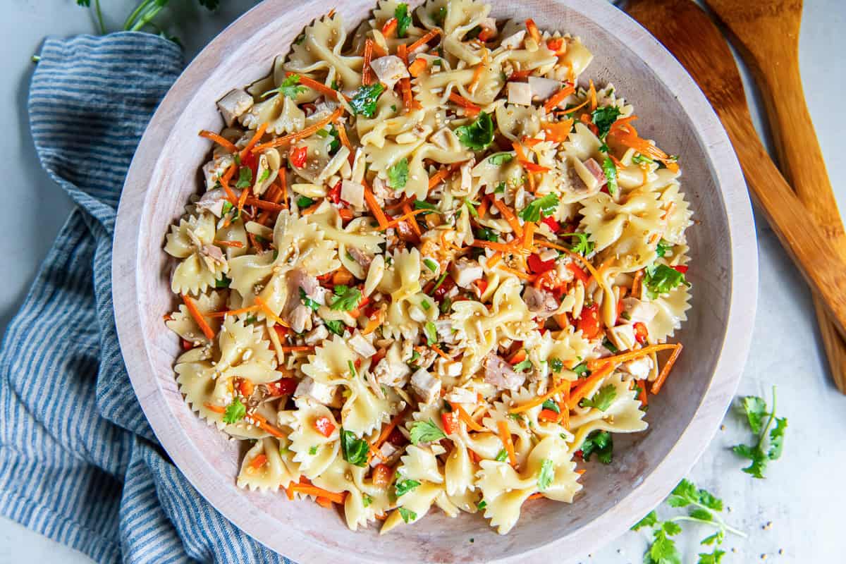 Asian Pasta Salad served in a wooden bowl with bowtie pasta, chicken, fresh vegetables, almonds, and sesame seeds.
