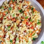 Asian Pasta Salad in a wooden serving bowl with chicken, bowtie pasta, fresh vegetables, almonds, and sesame seeds.