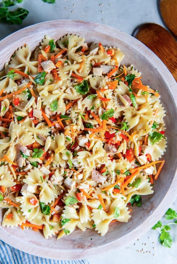 Asian Pasta Salad in a wooden serving bowl with chicken, bowtie pasta, fresh vegetables, almonds, and sesame seeds.