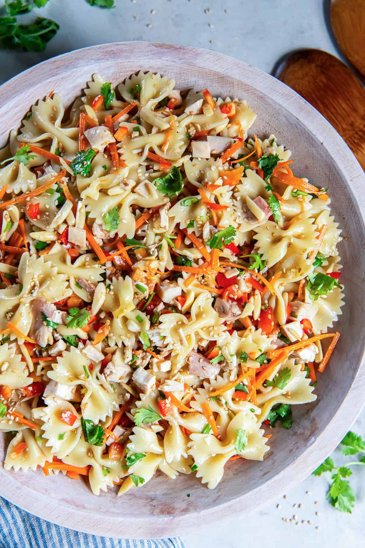 Asian Pasta Salad in a wooden serving bowl with chicken, bowtie pasta, fresh vegetables, almonds, and sesame seeds.