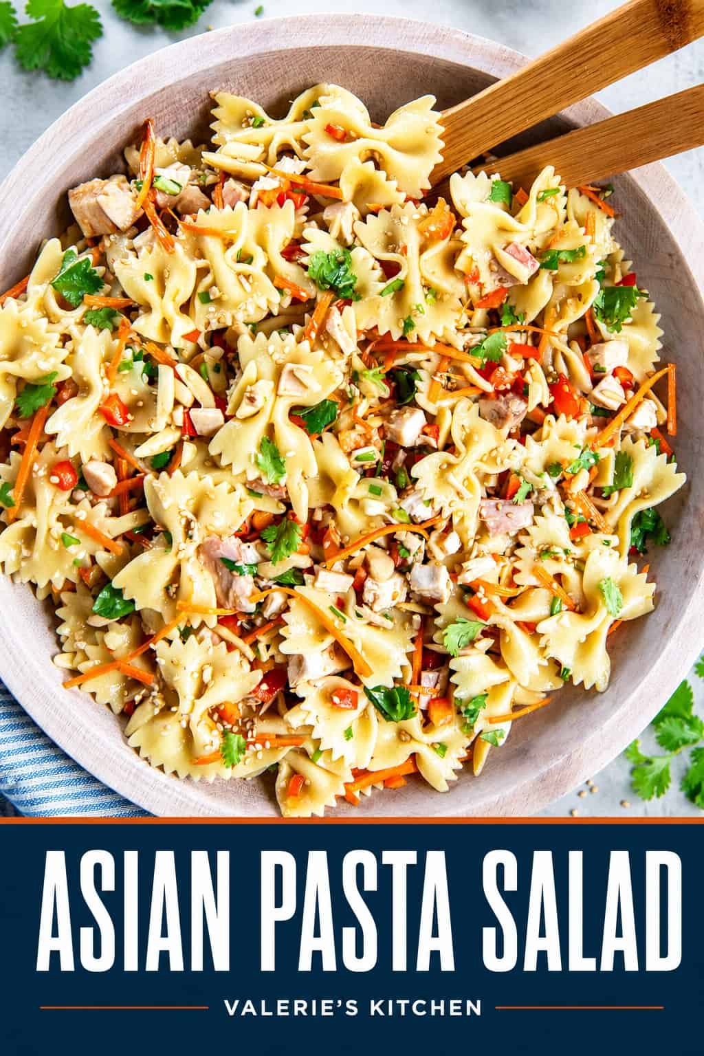 Asian Pasta Salad with bowtie pasta, chicken, carrots, red bell pepper, cilantro, and almonds in a wooden bowl with wooden salad servers with bold text overlay.