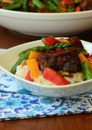 A plate of bbq ribs over rice with vegetables.