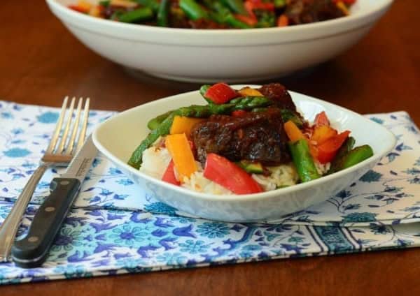 A plate of bbq ribs over rice with vegetables.