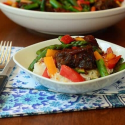 A plate of bbq ribs over rice with vegetables.