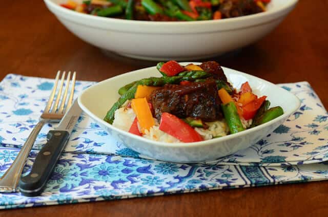 A plate of bbq ribs over rice with vegetables.