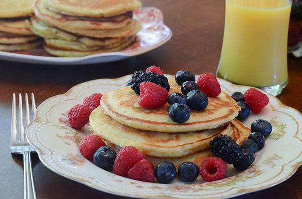 A serving of Mom's Buttermilk Pancakes with berries and a side of orange juice..