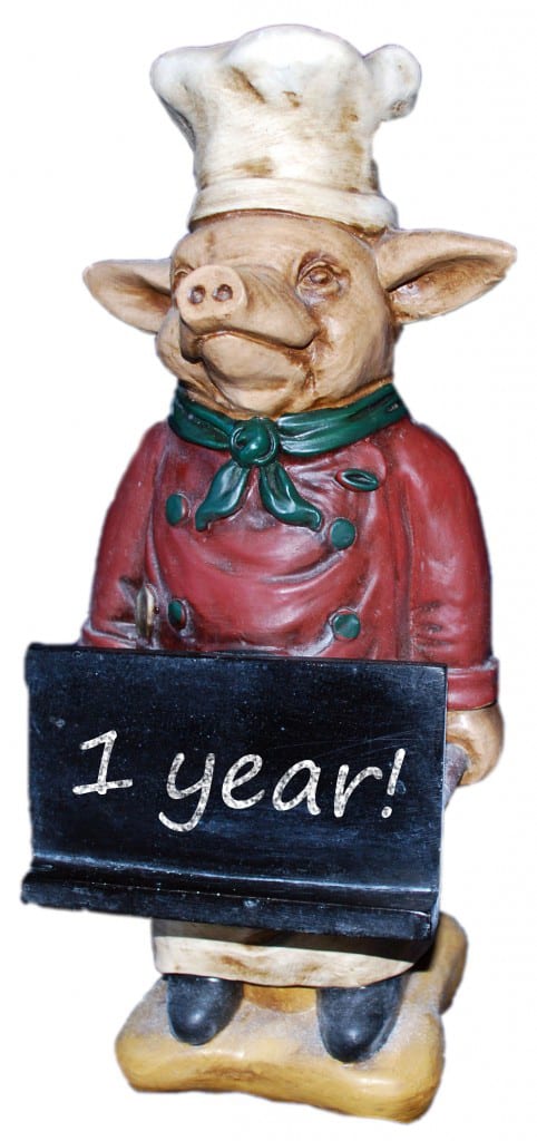 A pig decorative statue holding a sign that says 1 year! on it.