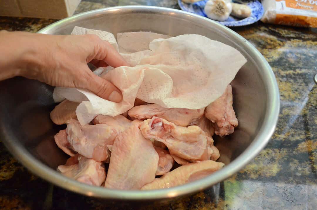 Chicken wings in a bowl being dried with a paper towerl.