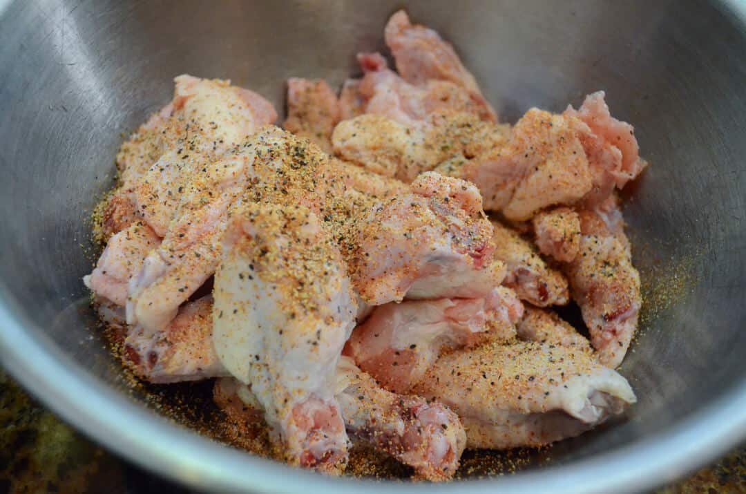 Chicken wings in a bowl being covered with seasoning.