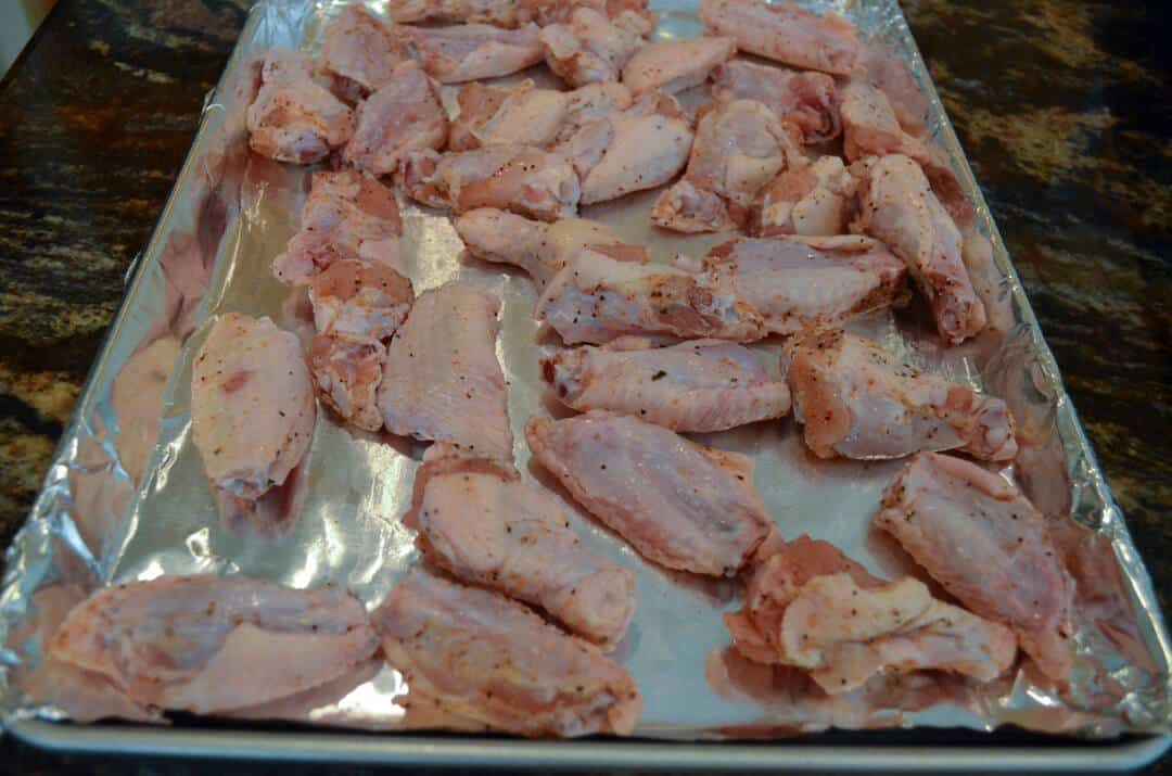 A foil lined baking sheet filled with seasoned chicken wings.