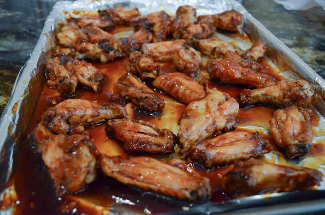 The chicken wings on the baking sheet covered in sauce.