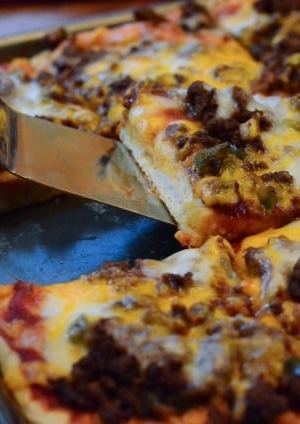 A close up of a spatula lifting a piece of pizza from a pan.
