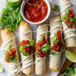 A top down shot of chicken taquitos on a board with salsa.