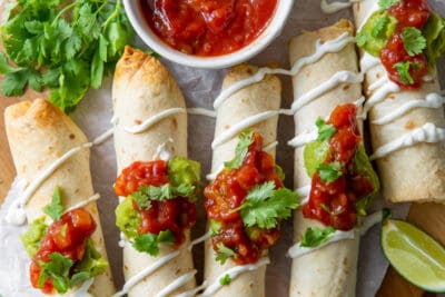 A top down shot of chicken taquitos on a board with salsa.