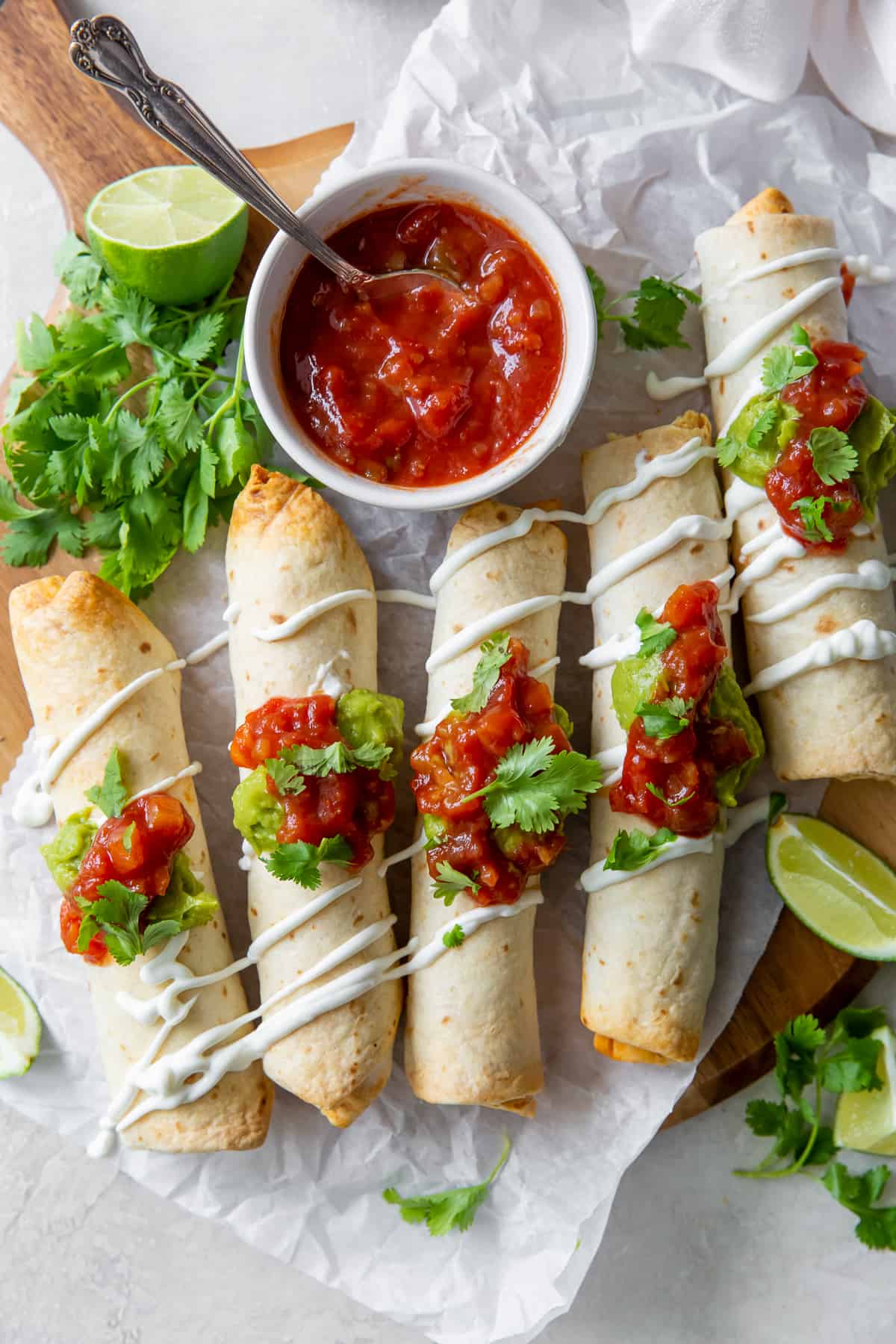 A top down shot of chicken taquitos on a board with salsa.