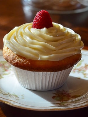 A cupcake with swirled frosting and a raspberry.