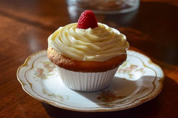 A cupcake with swirled frosting and a raspberry.