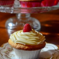 A cupcake with swirled frosting and a raspberry.