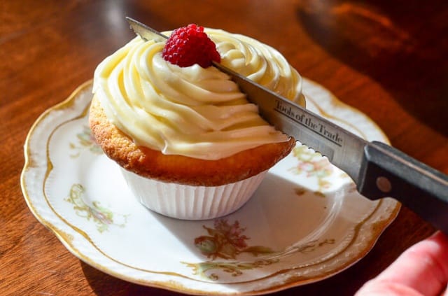 A Lemon Raspberry Cupcake with Lemon Curd Frosting is being cut in half.