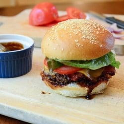 A hamburger with barbecue sauce and bacon on a wood board.