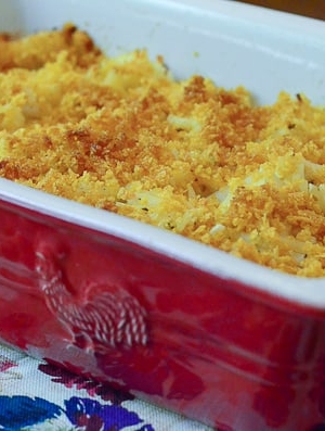 A red casserole dish full of cheesy hash browns with a browned topping.