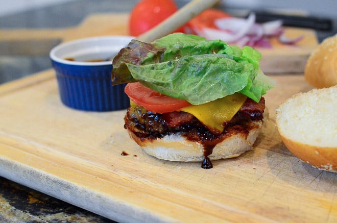 Assembling the Stout & Sriracha Barbecue Bacon Burgers on a wood cutting board.