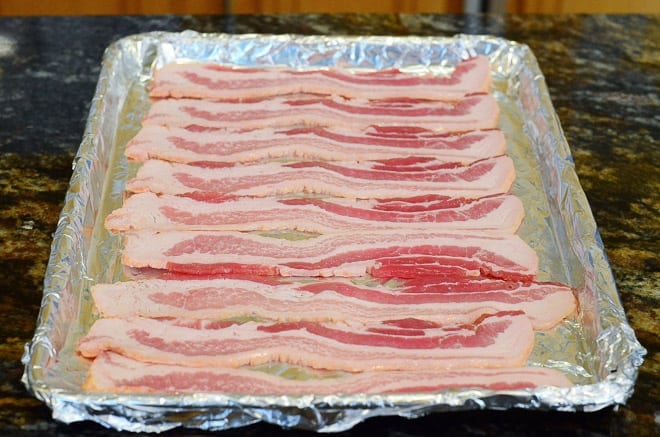 Uncooked bacon on a foil lined baking sheet.