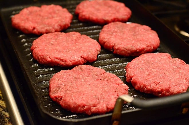 Burger patties cooking on a stove top grill.