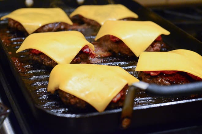 Stout & Sriracha Barbecue Bacon Burgers cooking on the grill with bacon and cheese on top.