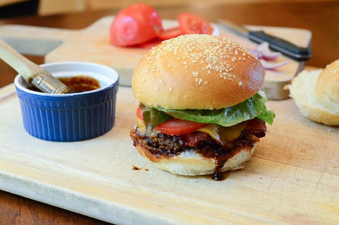 Stout & Sriracha Barbecue Bacon Burgers - on a cutting board with extra sauce in a small dish.
