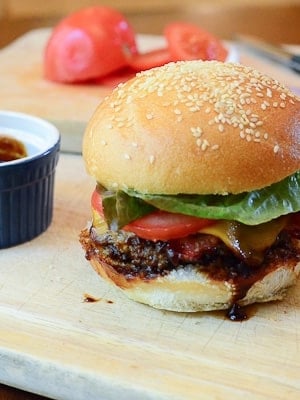 A hamburger with barbecue sauce and bacon on a wood board.