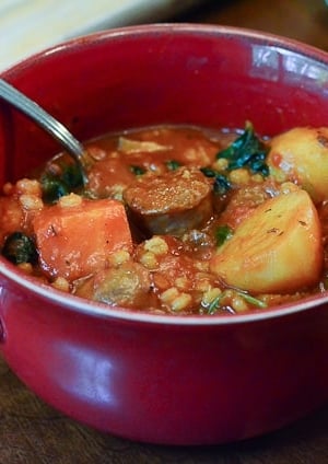 A bowl of sausage and barley stew with a spoon.