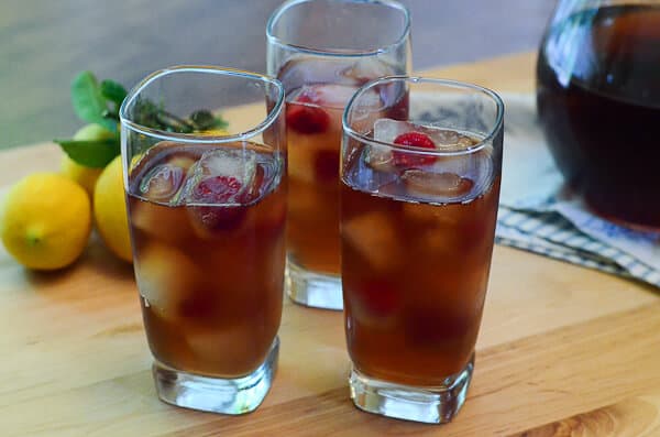 Three glasses of iced tea and lemonade with ice cubes and raspberries.