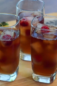 Three glasses of iced tea and lemonade with ice cubes and raspberries.