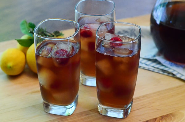 Three glasses of iced tea and lemonade with ice cubes and raspberries.
