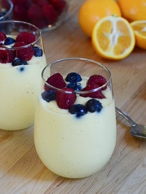 Two smoothies topped with fresh berries on a wood board.