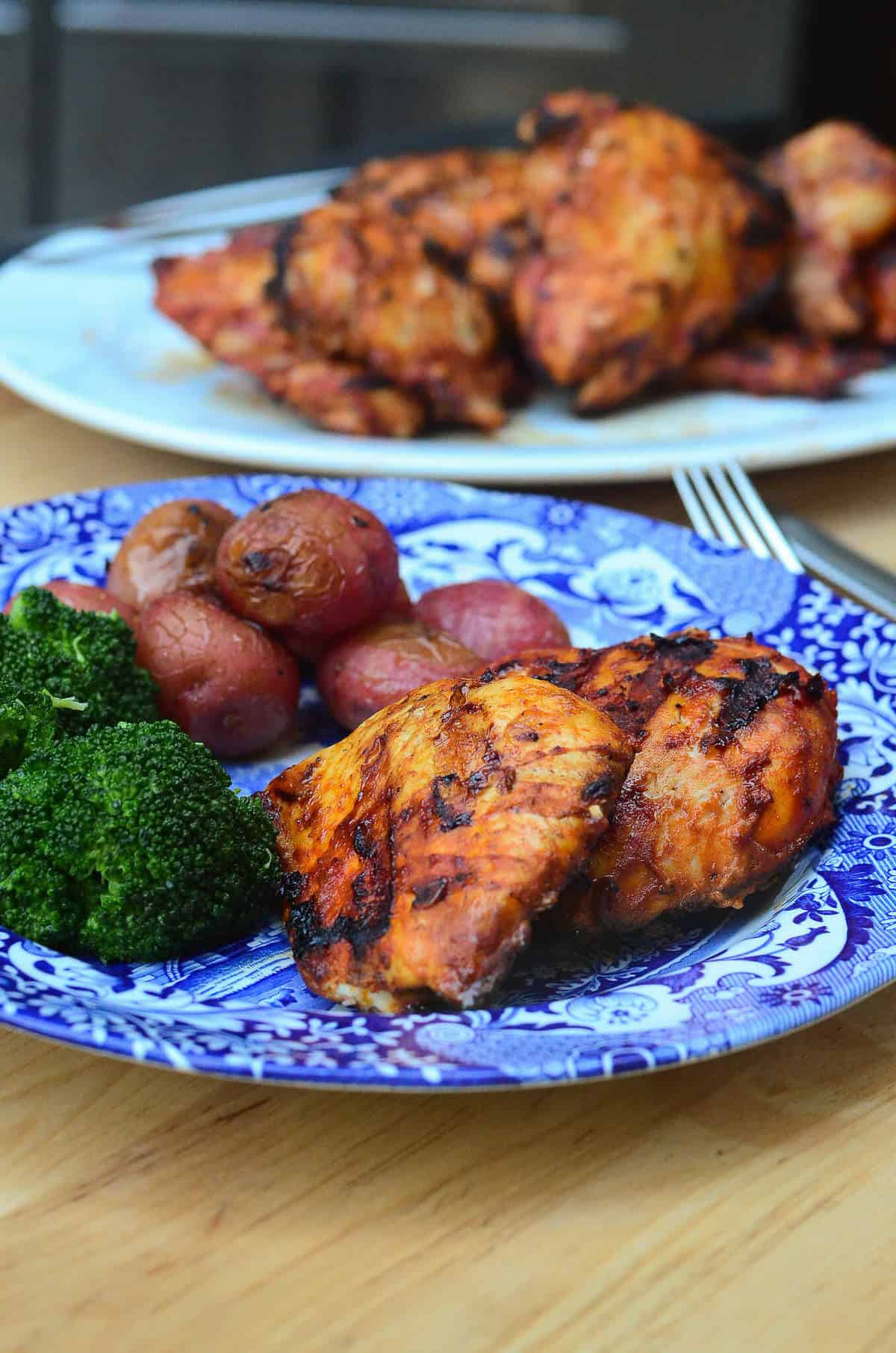 Grilled paprika chicken on a blue plate with broccoli and potatoes.