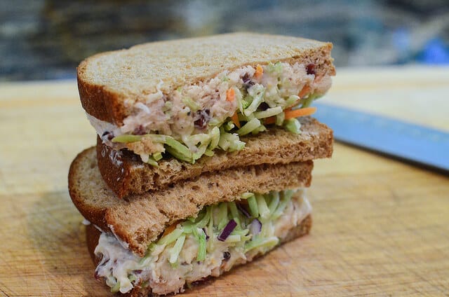 A chicken salad sandwich sliced in half and stacked on a cutting board.