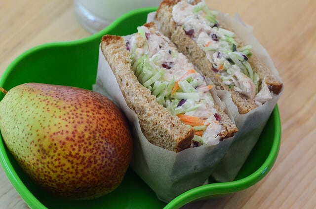 A sandwich and a pear in a green container.