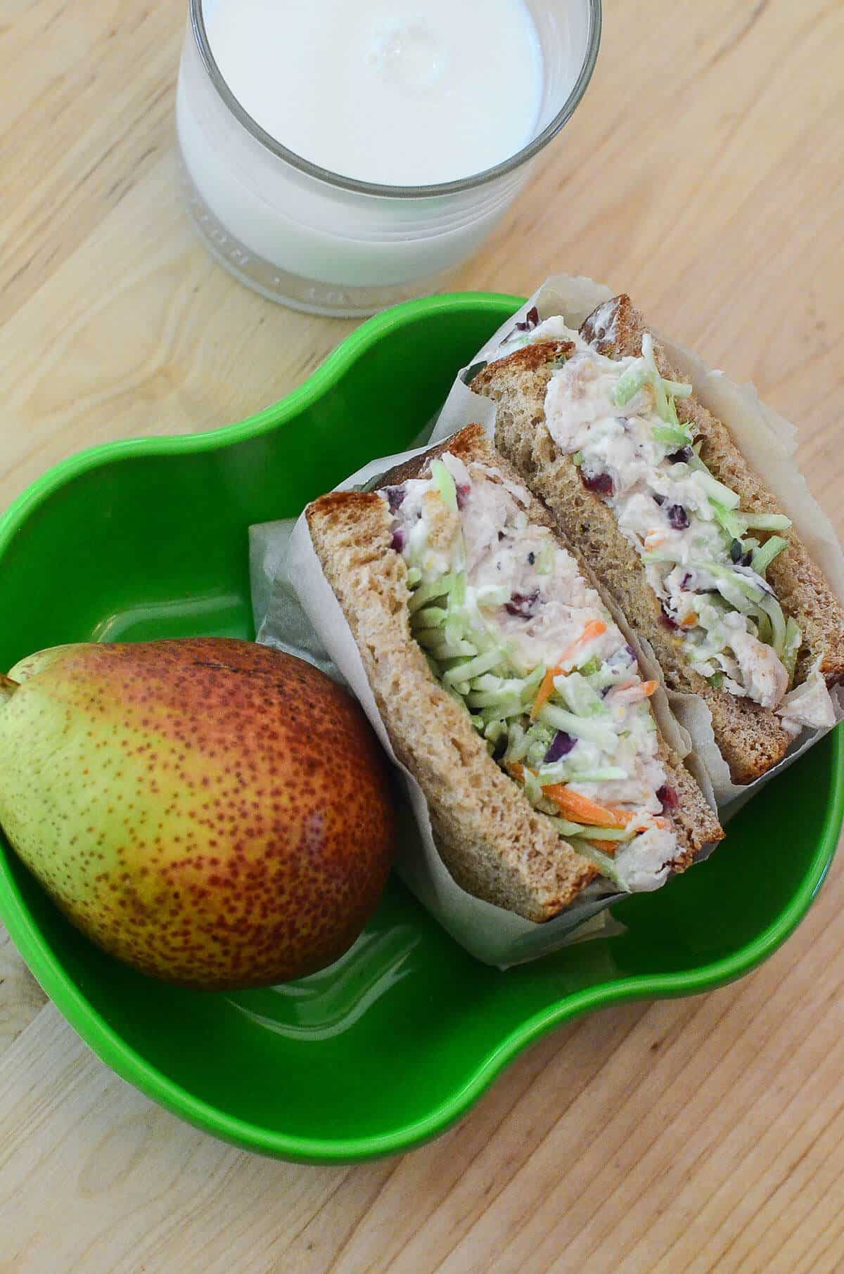A chicken salad sandwich with broccoli slaw in a green container shot from above.
