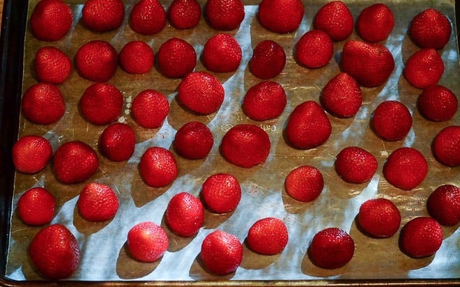 The strawberries are placed on wax paper lined baking sheet.