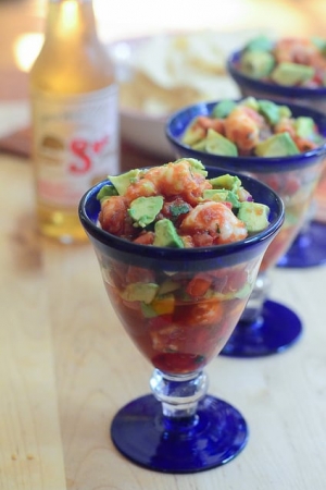 Shrimp and pieces of avocado in cocktail sauce in a glass.