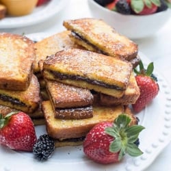 Nutella French Toast Sticks stacked on a plate with berries.