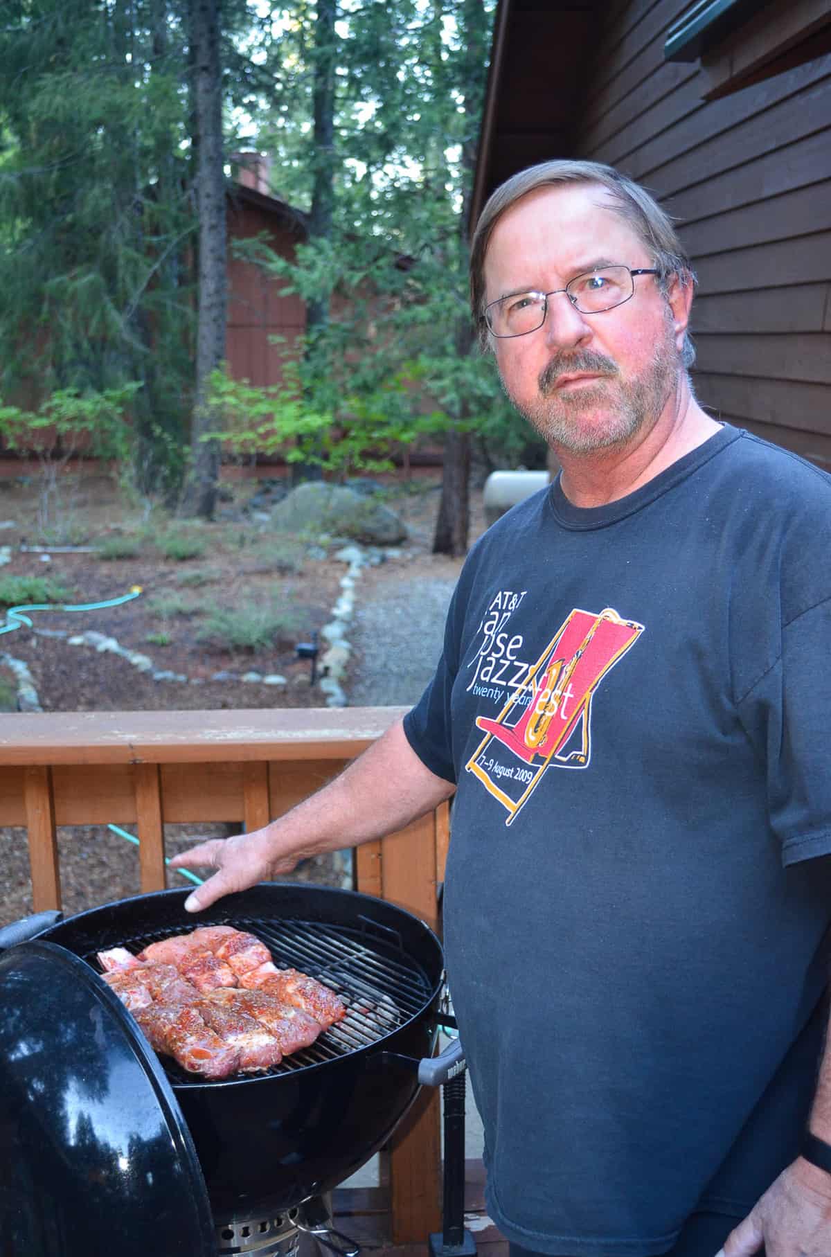 A man holds his hand towards Country Style Ribs on a Weber BBQ.
